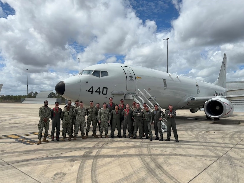 A group of U.S. and Australian sailors stand for a photo in front of a small aircraft.