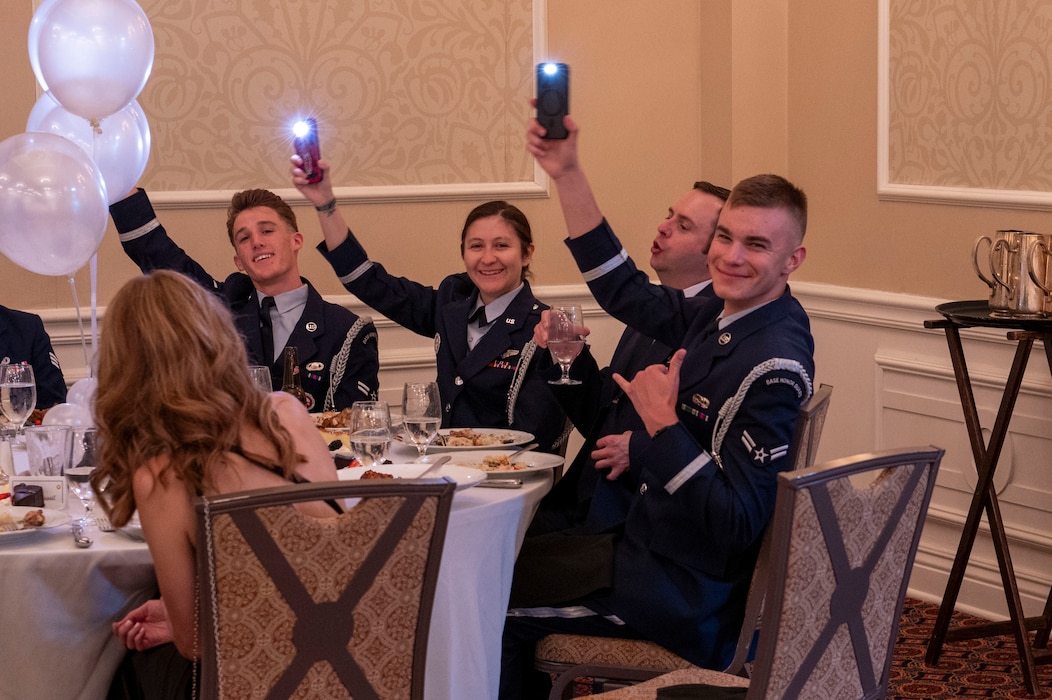 air force members dressed in blues use their phone flashlights as candles