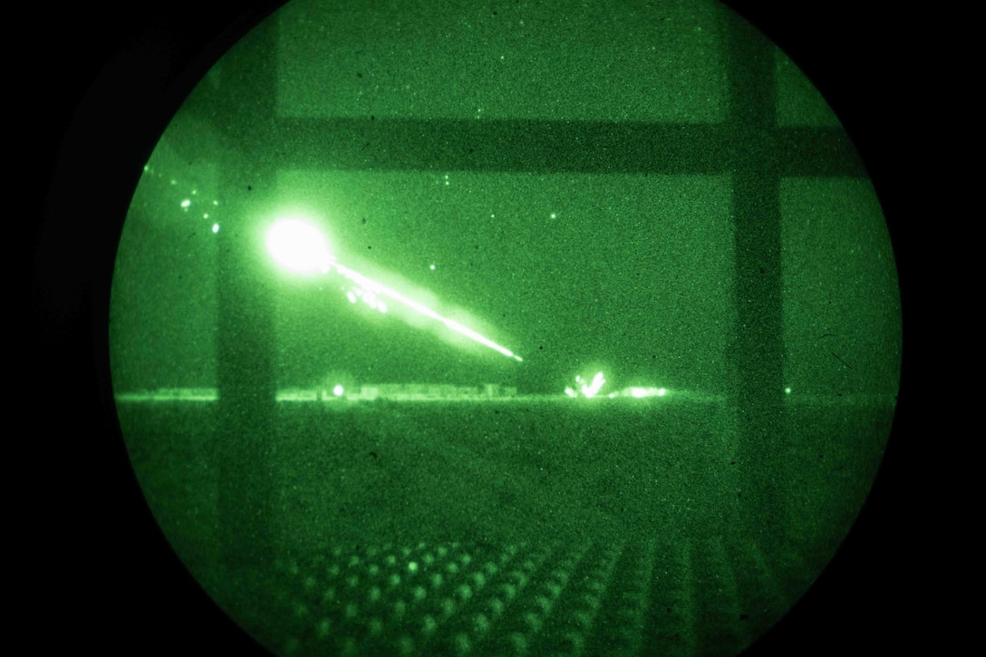 A helicopter fires missiles at a target in a night vision photo taken through a round scope.