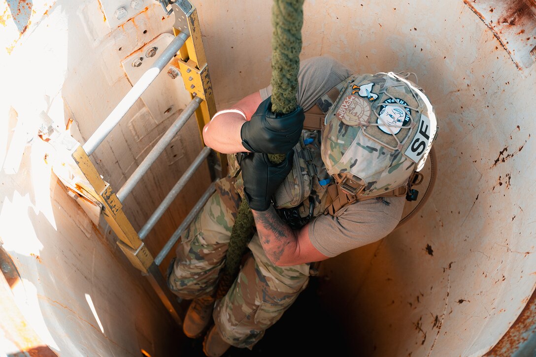 An airman fast-ropes down a large tube with a ladder position to the side.