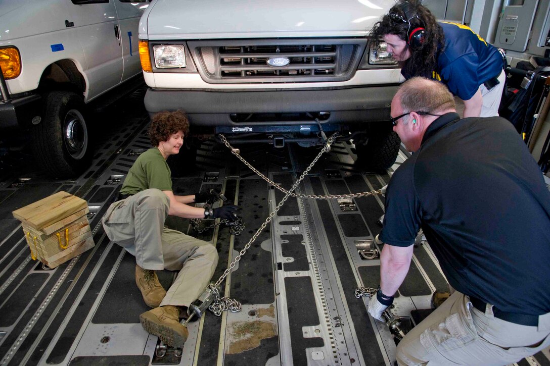 People chain down a vehicle in an aircraft.