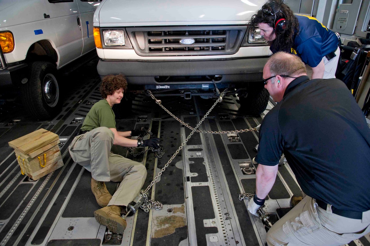 People chain down a vehicle in an aircraft.