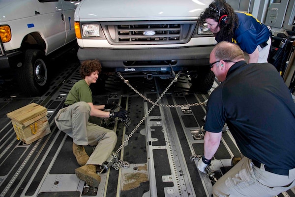 People chain down a vehicle in an aircraft.