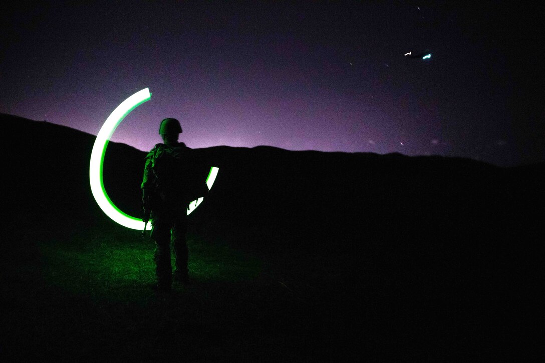 A soldier swings a chem light outside at night.
