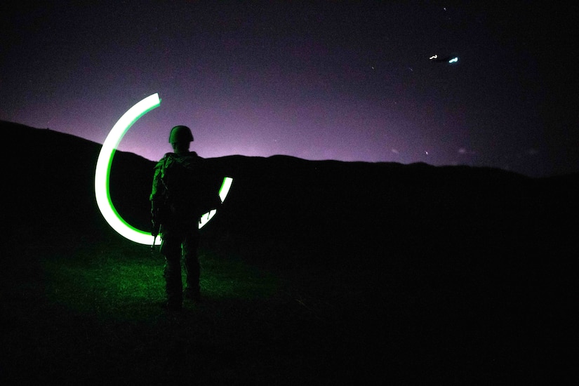 A soldier swings a chem light outside at night.