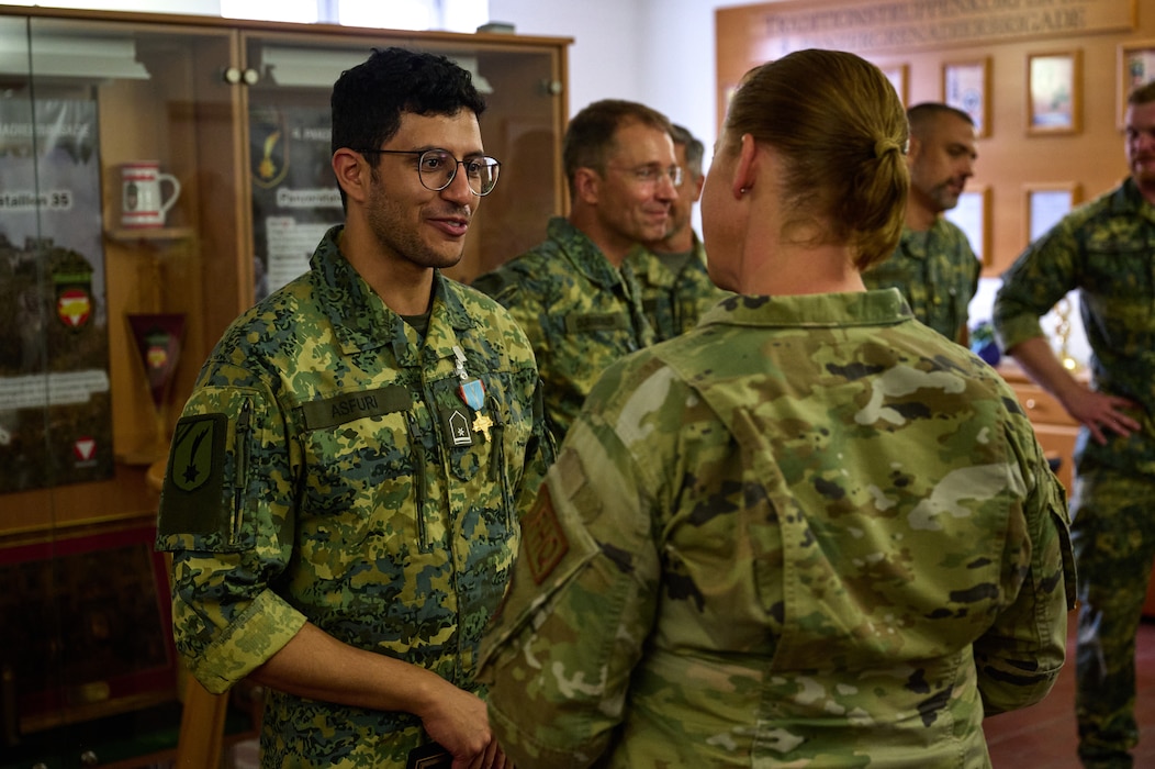 An Austrian service member talks with a U.S. service member inside a room with other service members.