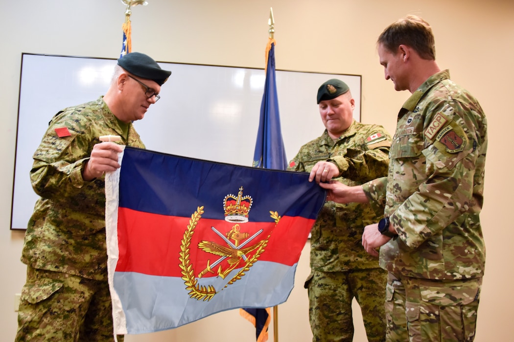 Two Canadian service members present a special commemorative flag to a U.S. Airman.