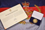 The Canadian Forces Unit Commendation award, pictured, is presented in three elements. The first part is a scroll inscribed with a citation in both official languages and signed by the chief of the Defense Staff. The second part is a twelve-sided gold-colored medallion bearing the symbols of the three services: the anchor, the crossed swords, and the flying eagle topped by the royal crown.