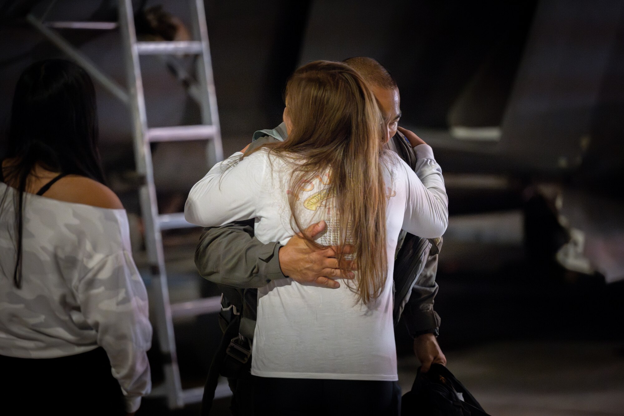 A pilot hugs a family member in front of a jet at night.