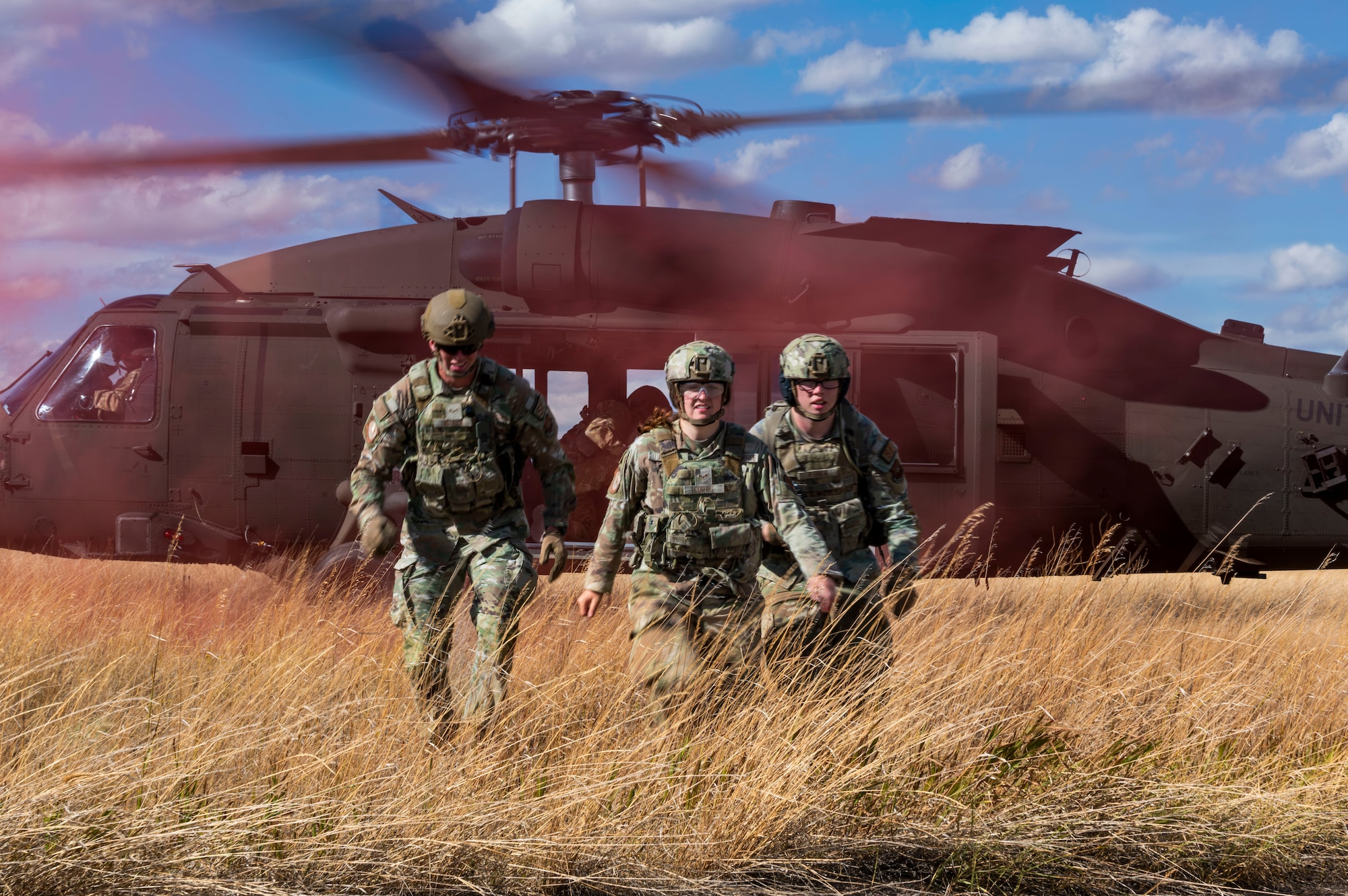 Three Airmen walking away from a helicopter in an open field.