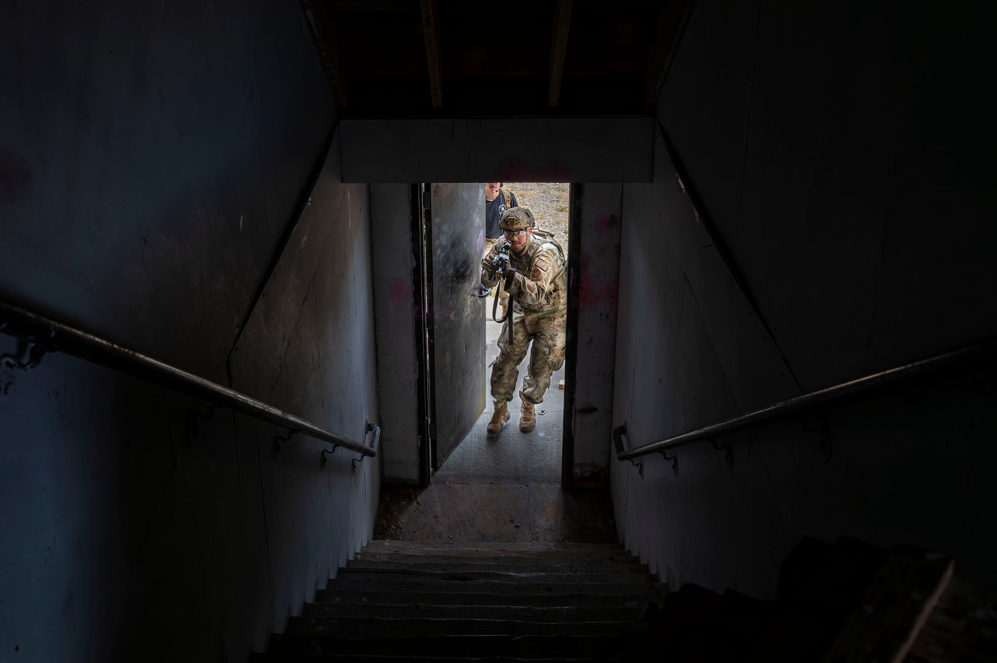 A dark stairwell pointed toward an open door with a military man blasting through.