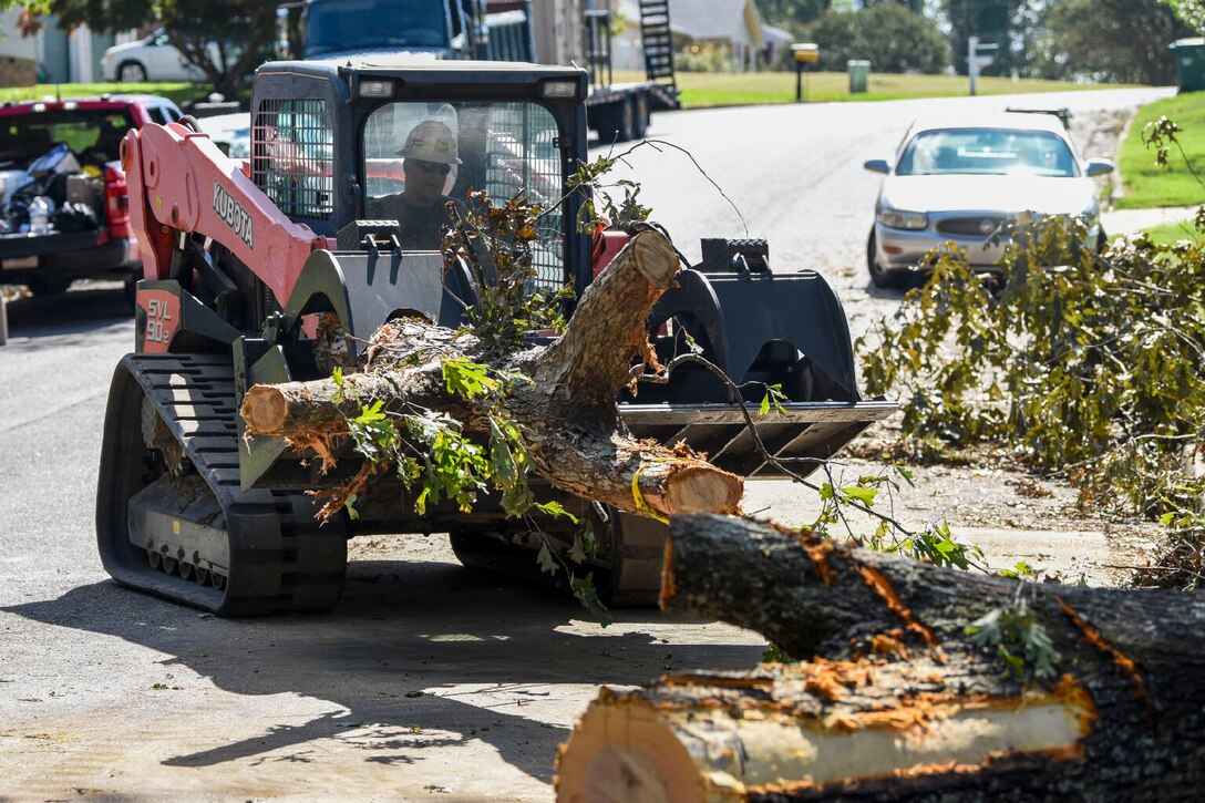 A large piece of equipment moves fallen trees off a roadway.