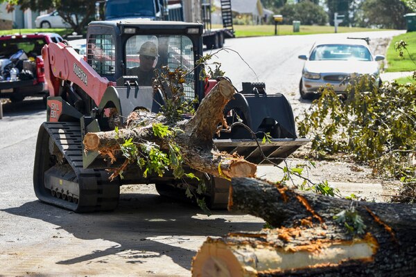 A large piece of equipment moves fallen trees off a roadway.