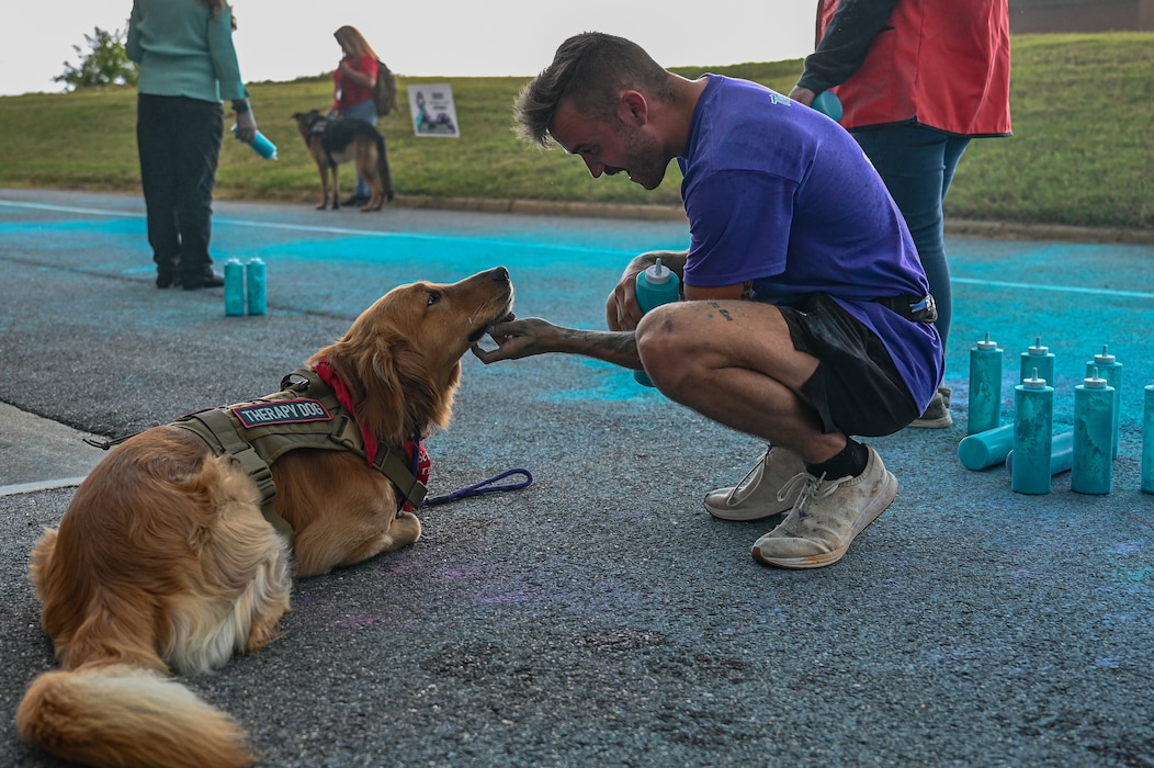Military OneSource support - Photo of an Airman scratching the bottom of a service dogs' neck in front of location in which participants were running in a color run race.