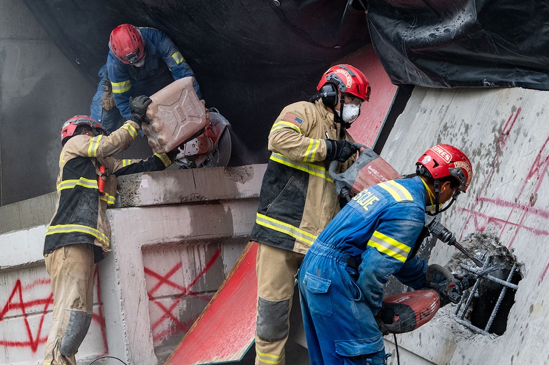 Four soldiers in helmets and masks lift objects and operate power tools in an urban search and rescue training.