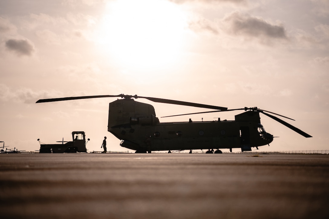 A soldier photographed in silhouette walks toward a military aircraft parked on a tarmac.