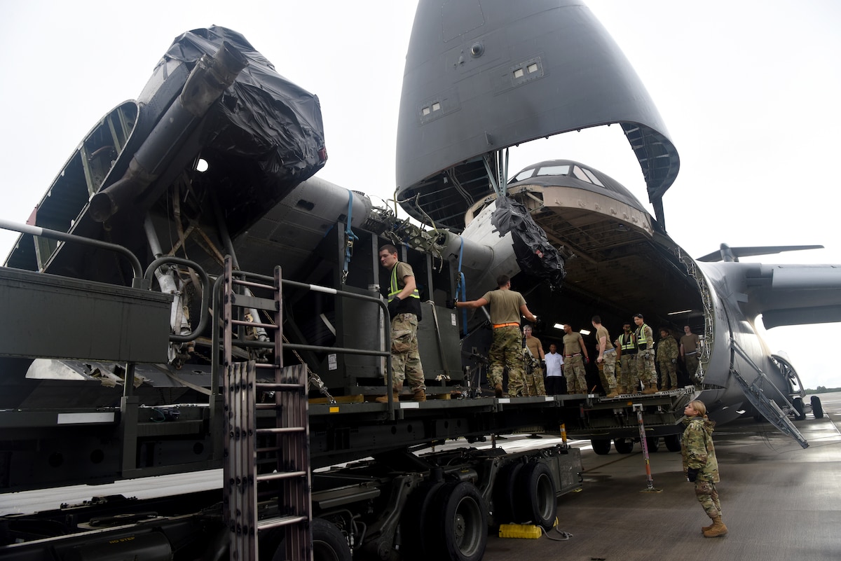 People in military uniforms unloading aircraft parts onto a trailer