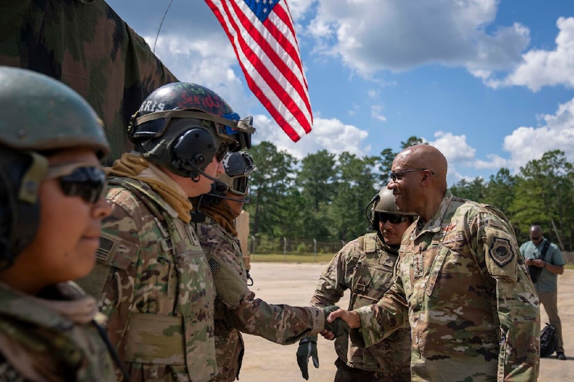 A military general greets soldiers during daylight. A United States flag flows behind them.