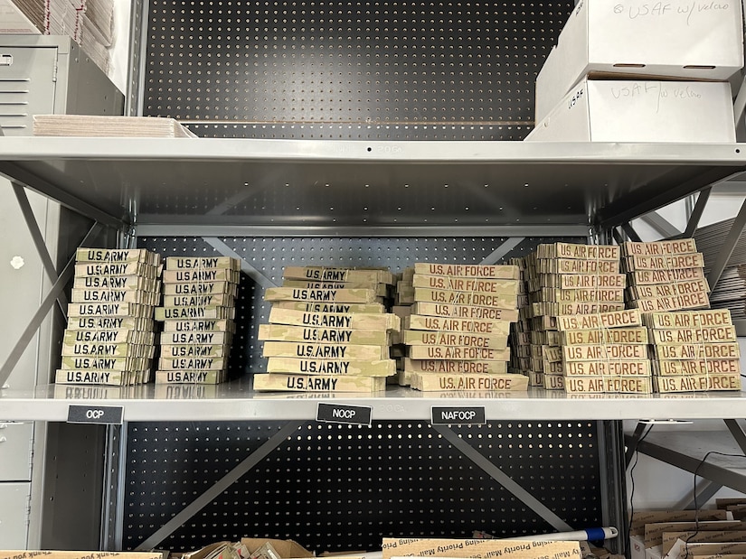 A shelf shows piles of name tapes with military branches stitched onto them.