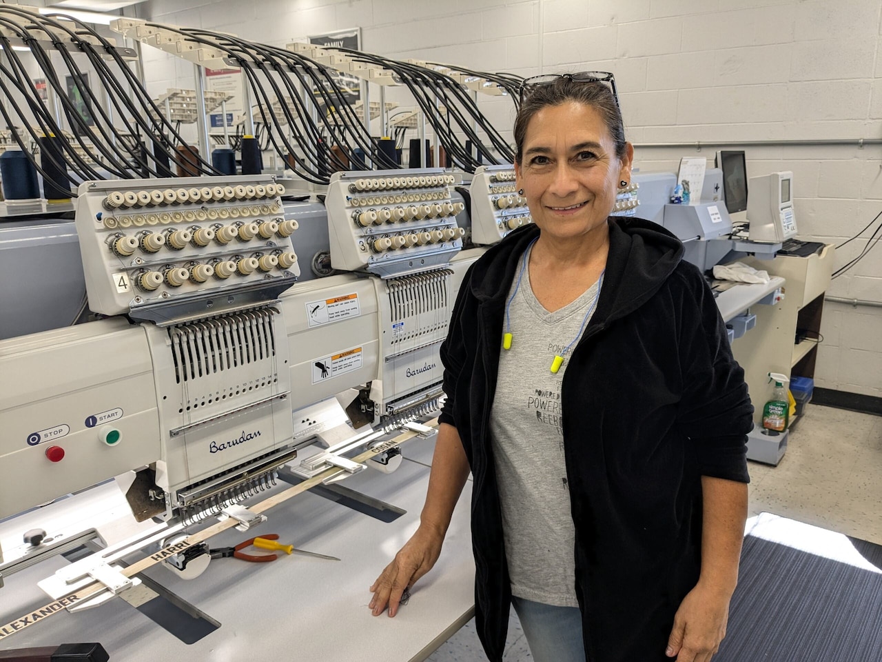 A woman poses for a photo in front of an automated sewing machine.