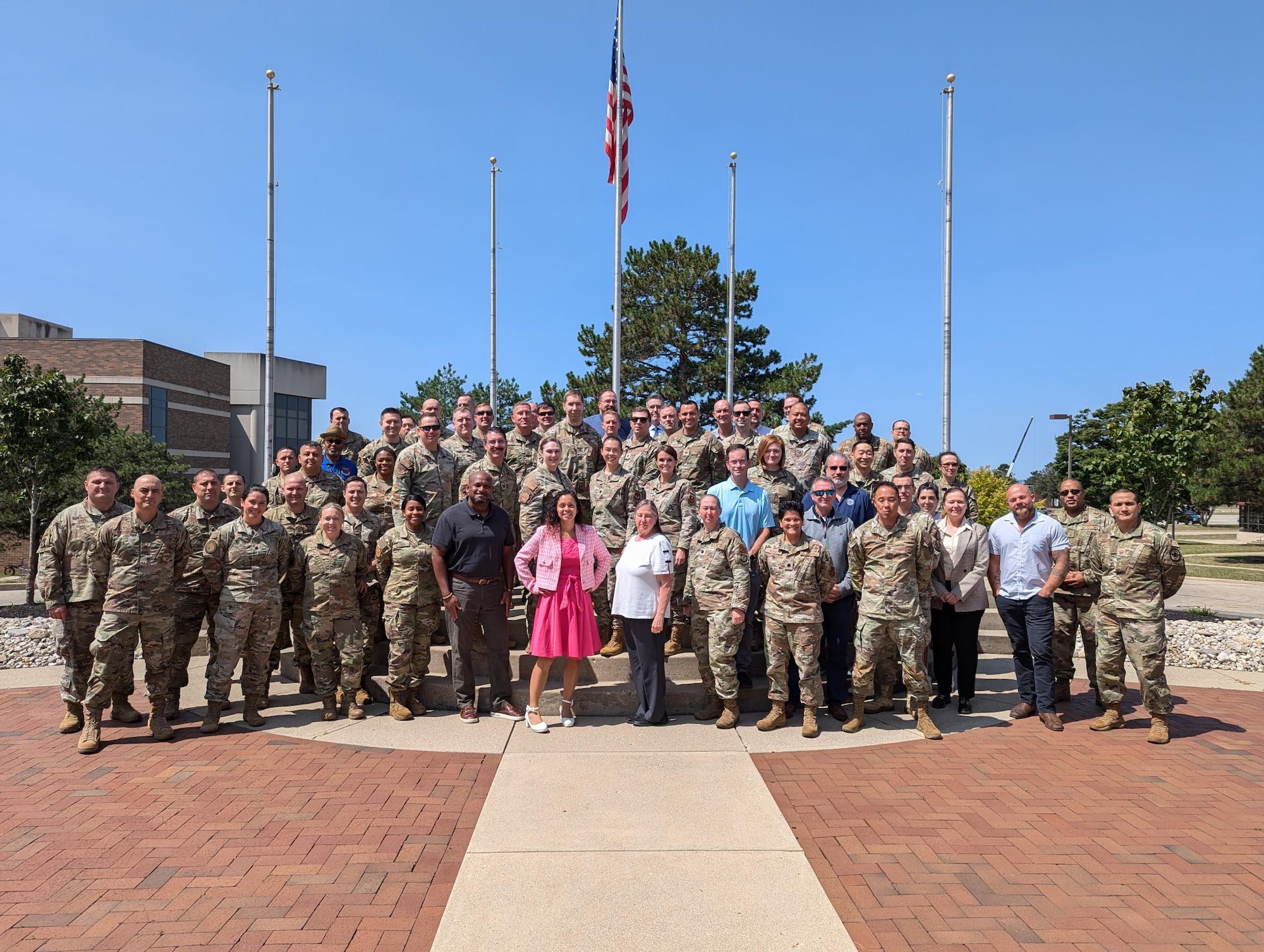 A group of military and civilians standing in front of an American Flag