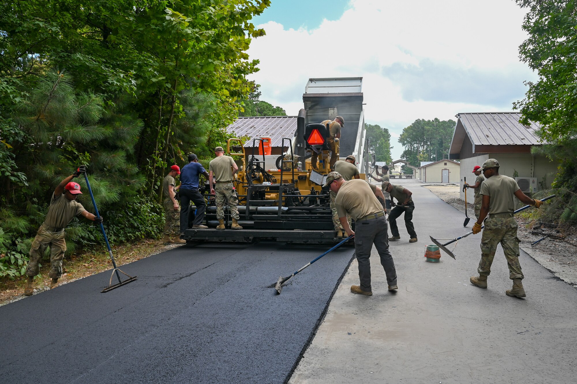Wide shot of Airmen working together with tools near a machine that lays down asphalt.