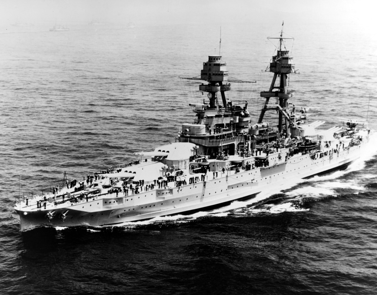 A battleship steams through the ocean in an aerial view.