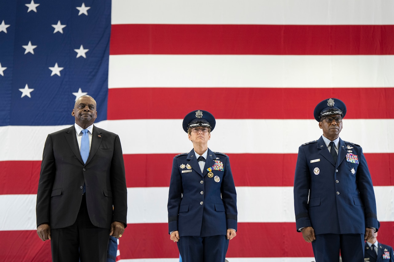 Three people stand in front of an American flag.