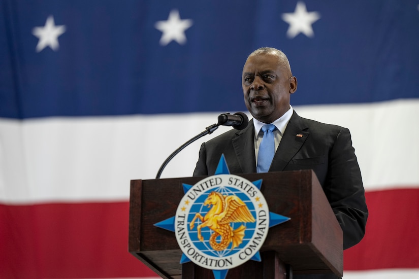 A man speaks from a podium while standing in front of an American flag.