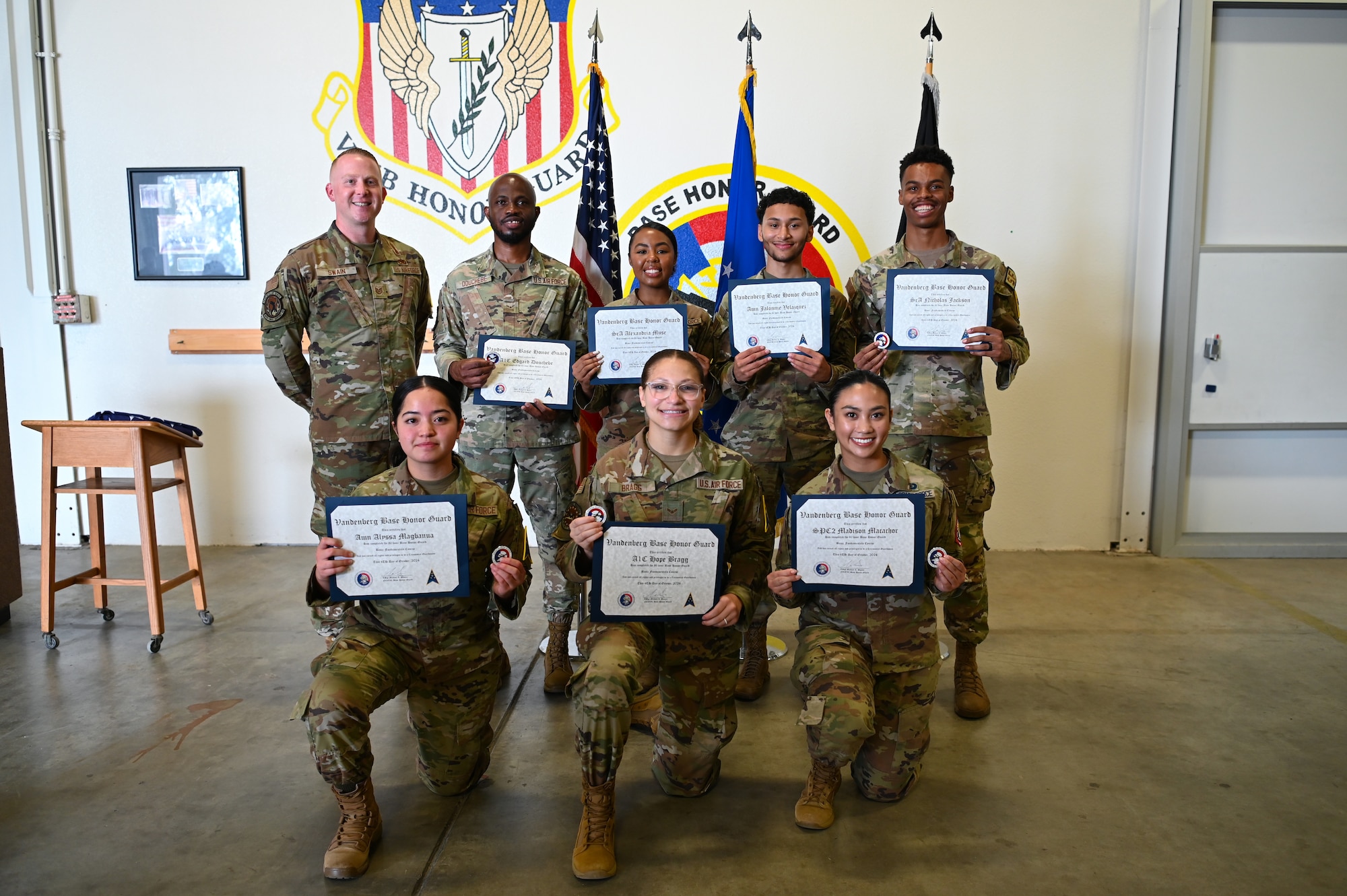 honor guard graduates standing with their certificates and smiling in front of us flag