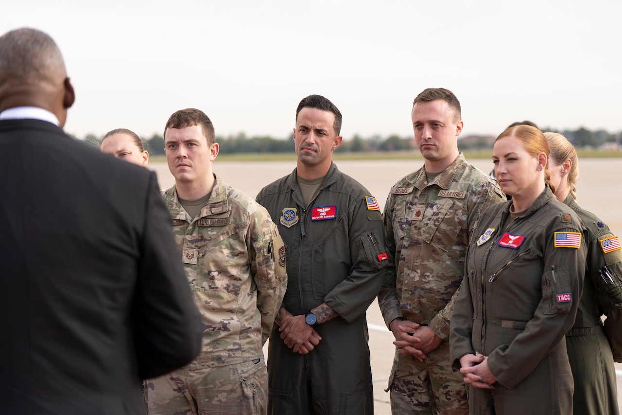 Secretary of Defense Lloyd J. Austin III, partly visible from behind, talks to troops facing him on a flight line.
