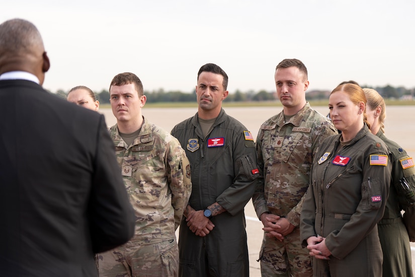 Secretary of Defense Lloyd J. Austin III, partly visible from behind, talks to troops facing him on a flight line.