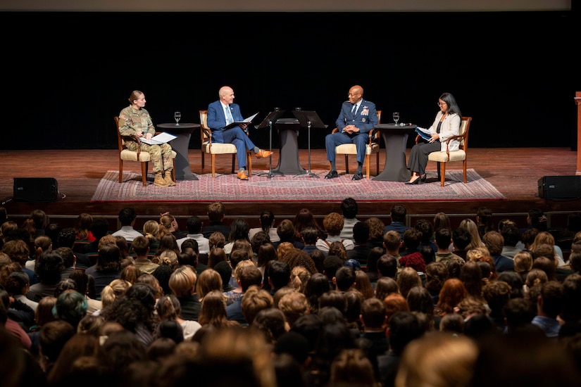 A group of people sit on chairs on a stage in front of an audience.