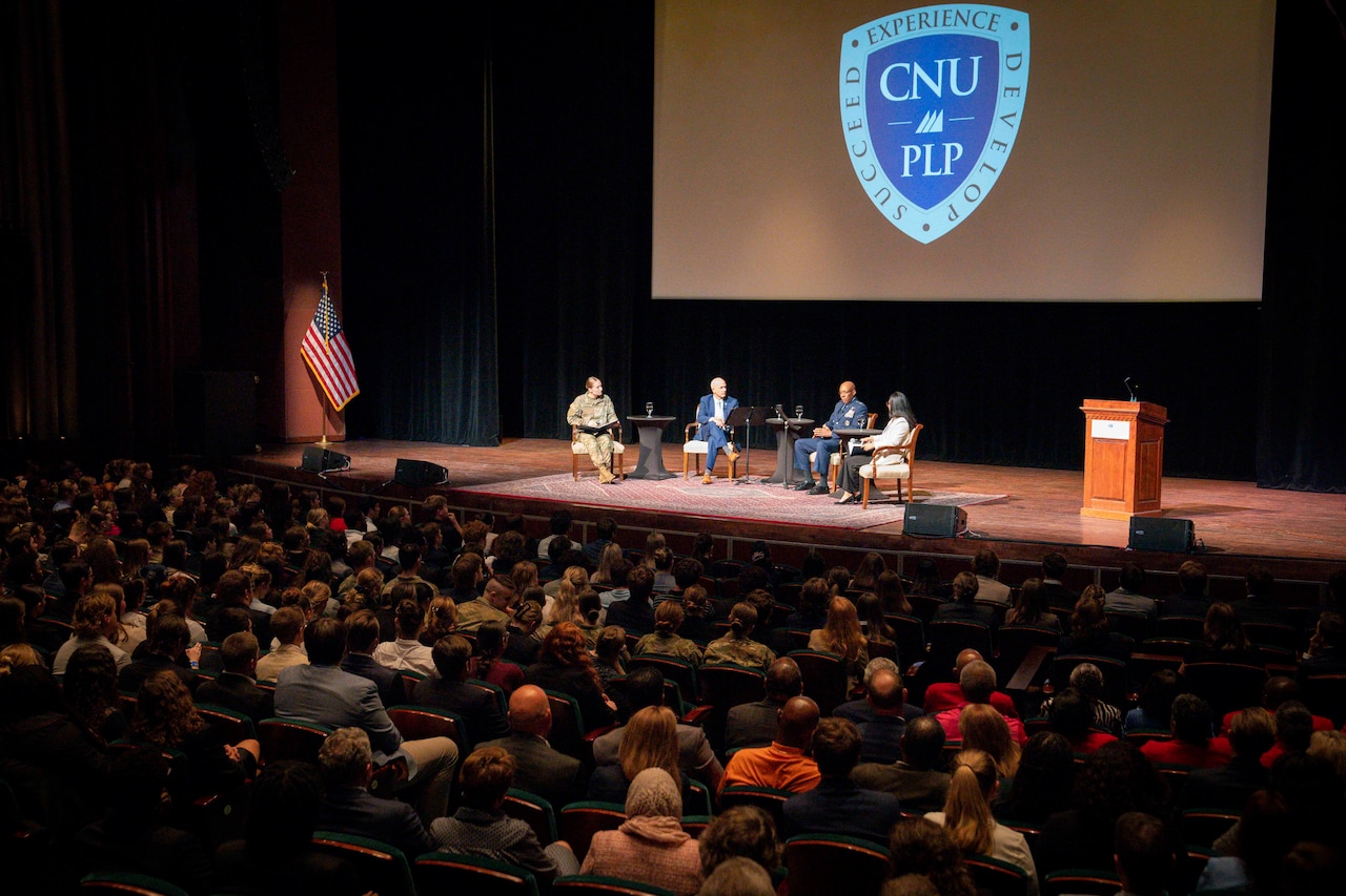 A group of people in chairs are seated on a stage in front of an audience of people.