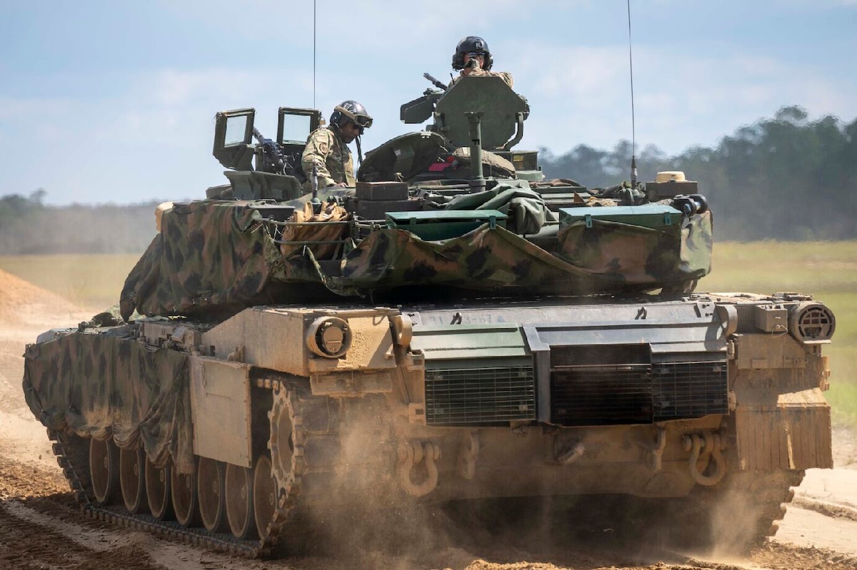 Two soldiers navigate a military vehicle on a dirt road.
