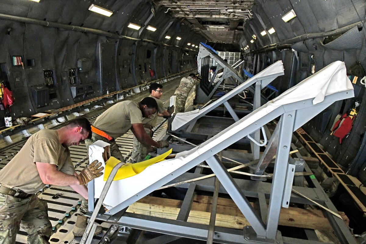 Men in military uniforms strapping down large metal parts inside aircraft