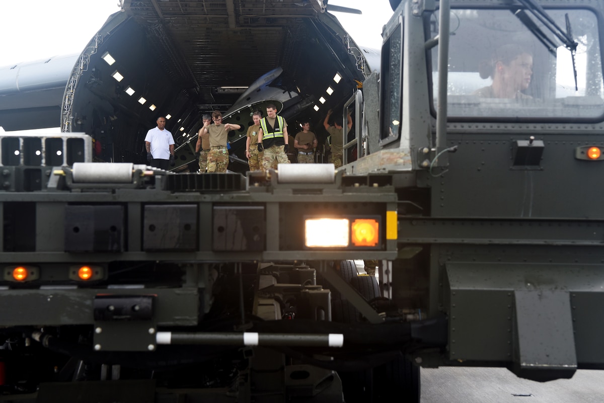 A flatbed truck backing up to the back of a large aircraft