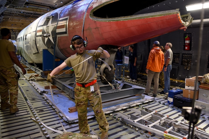 A man in a military uniform undoing straps on an aircraft part