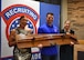 3 Army Soldiers in civilian attire smile while holding a large award in front of a Recruiting Brigade backdrop