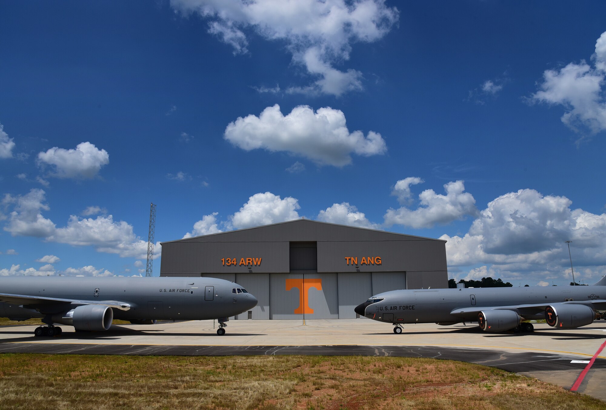 A KC-46 Pegasus and a KC-135R Stratotanker are parked in front of a new hangar bearing an orange 'T'