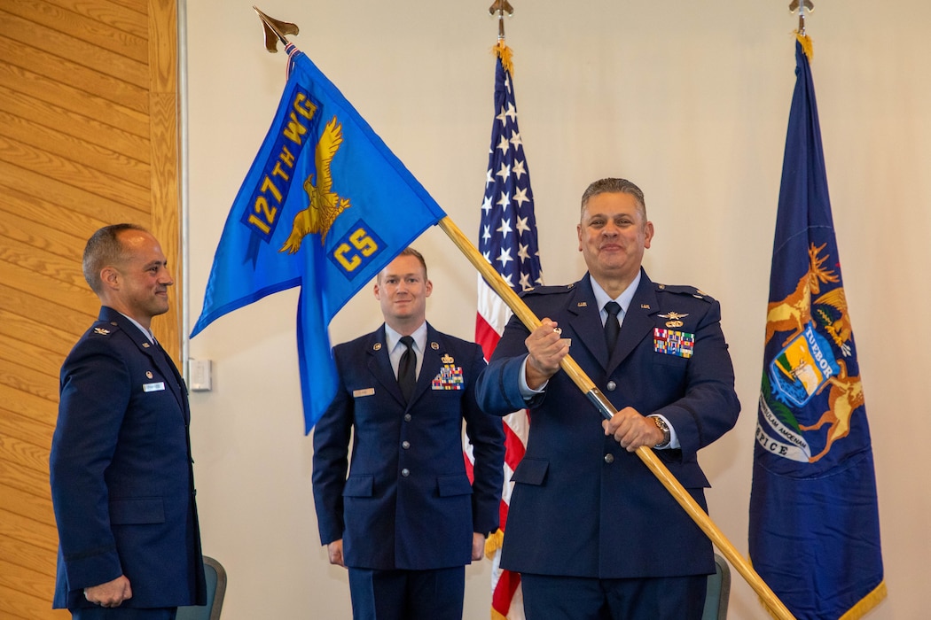 Male Air Force officer in dress blue uniform, presents unit flag.