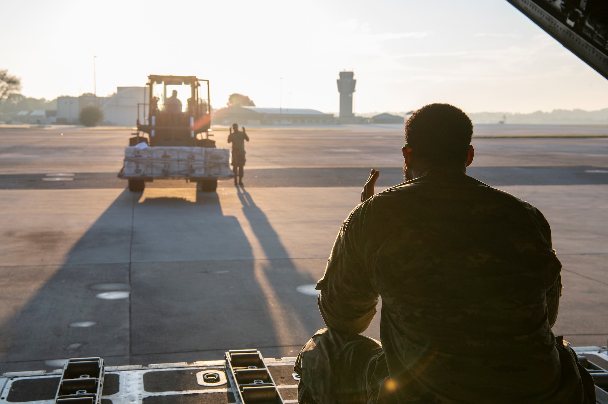 Airmen serve as spotters for a forklift carrying simulated cargo as it moves to the back of an aircraft.