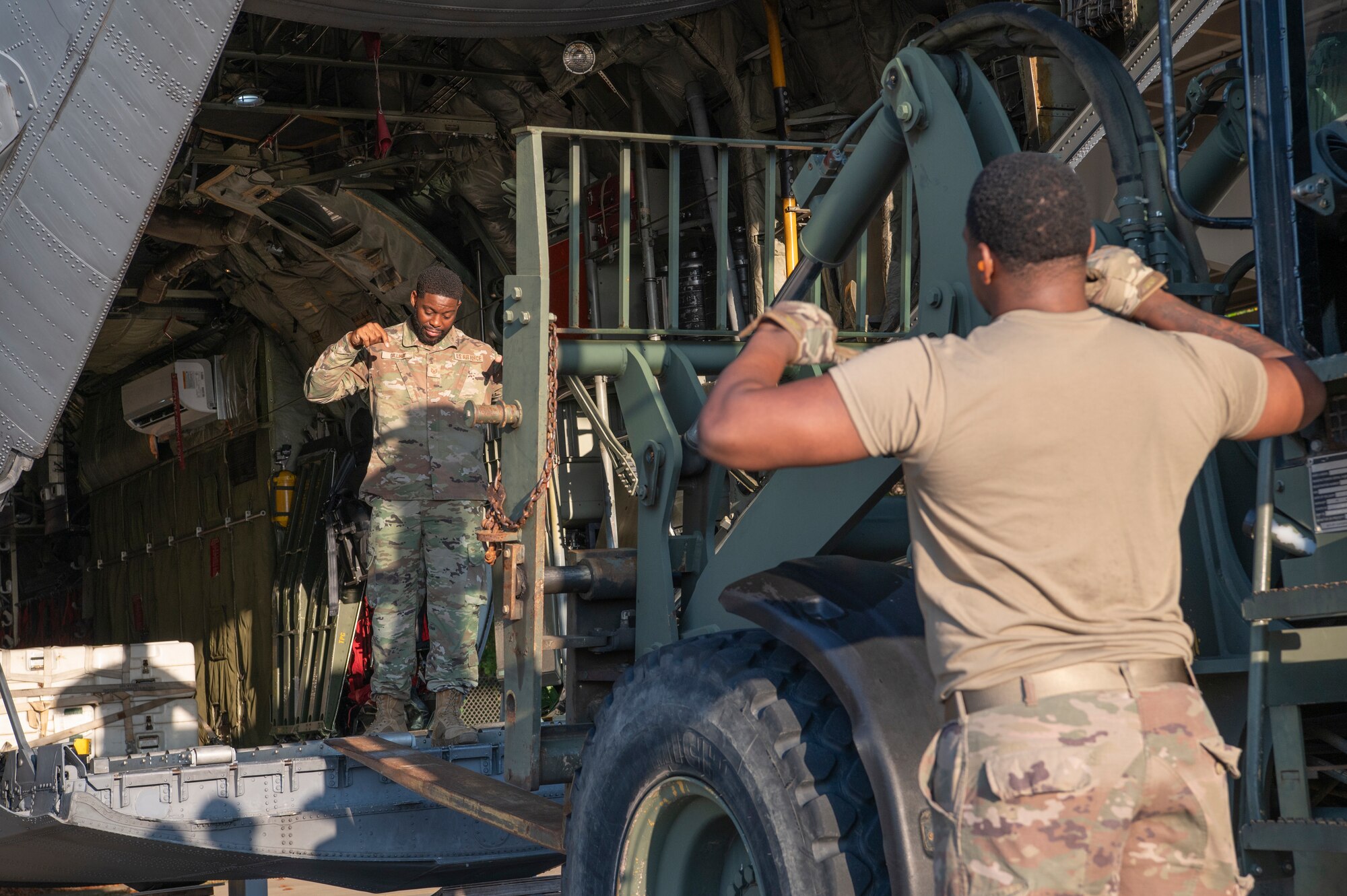 Two airmen help spot a forklift operator as the forklift's tines enter the back of an aircraft.