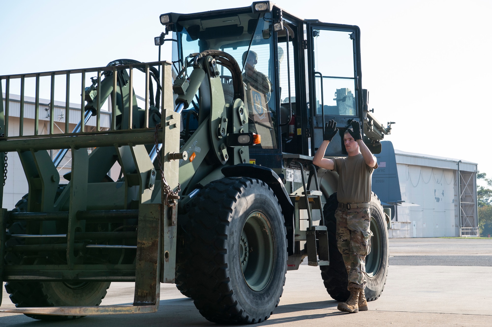 An airmen helps guide a forklift to aircraft.