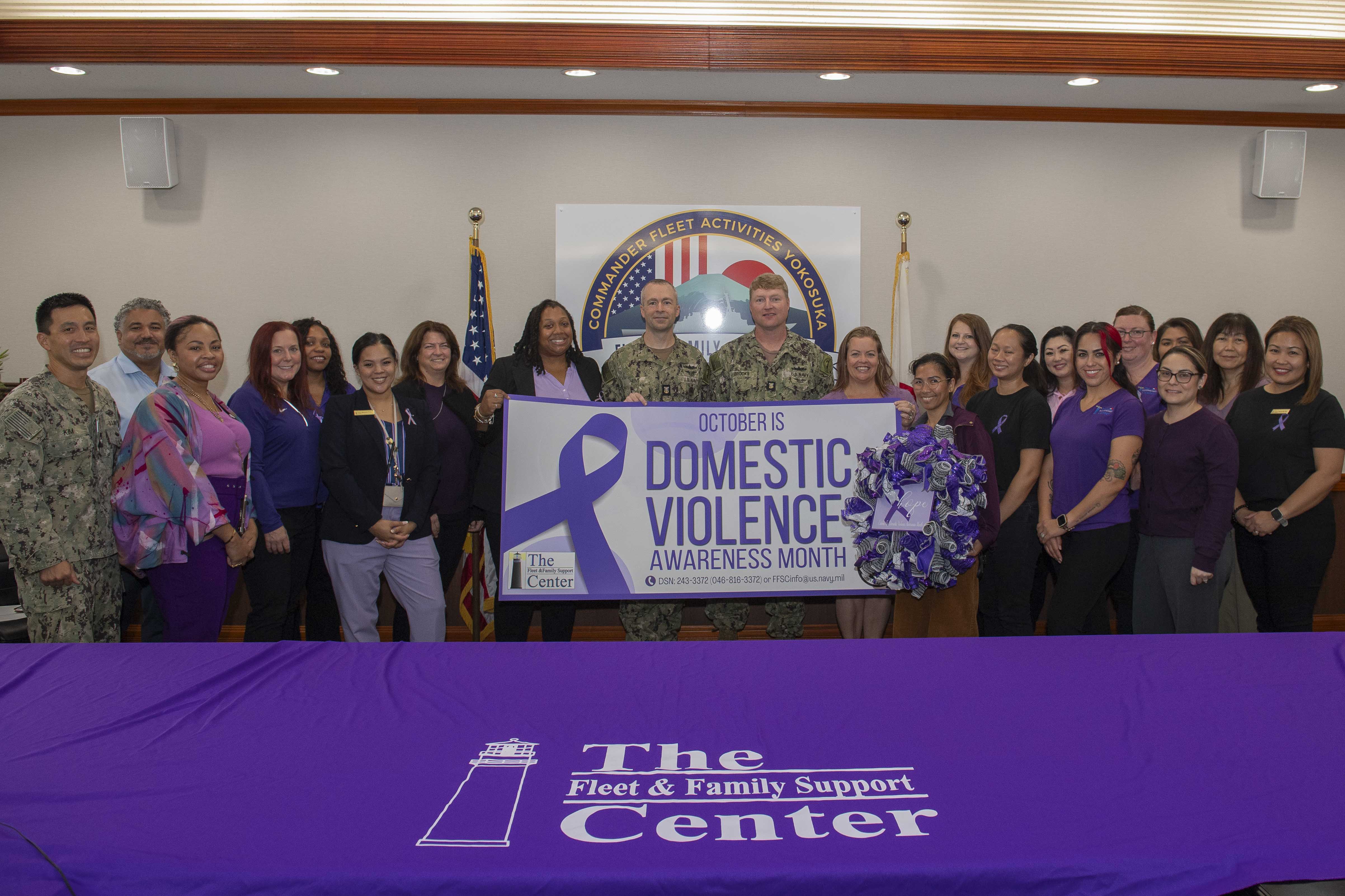 Command Master Chief Dennis Hunt, center left, and Master Chief Boatswain's Mate Jeffrey Brooks, center right, pose for a photo with employees and volunteers of the Fleet and Family Support Center (FFSC), during the FFSC Domestic Violence Proclamation Signing event for Domestic Violence Awareness Month at Commander, Fleet Activities Yokosuka’s headquarters.