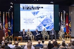 A group of people are seated on stage. They have papers in front of them and are all in business attire. There are two women and four men.