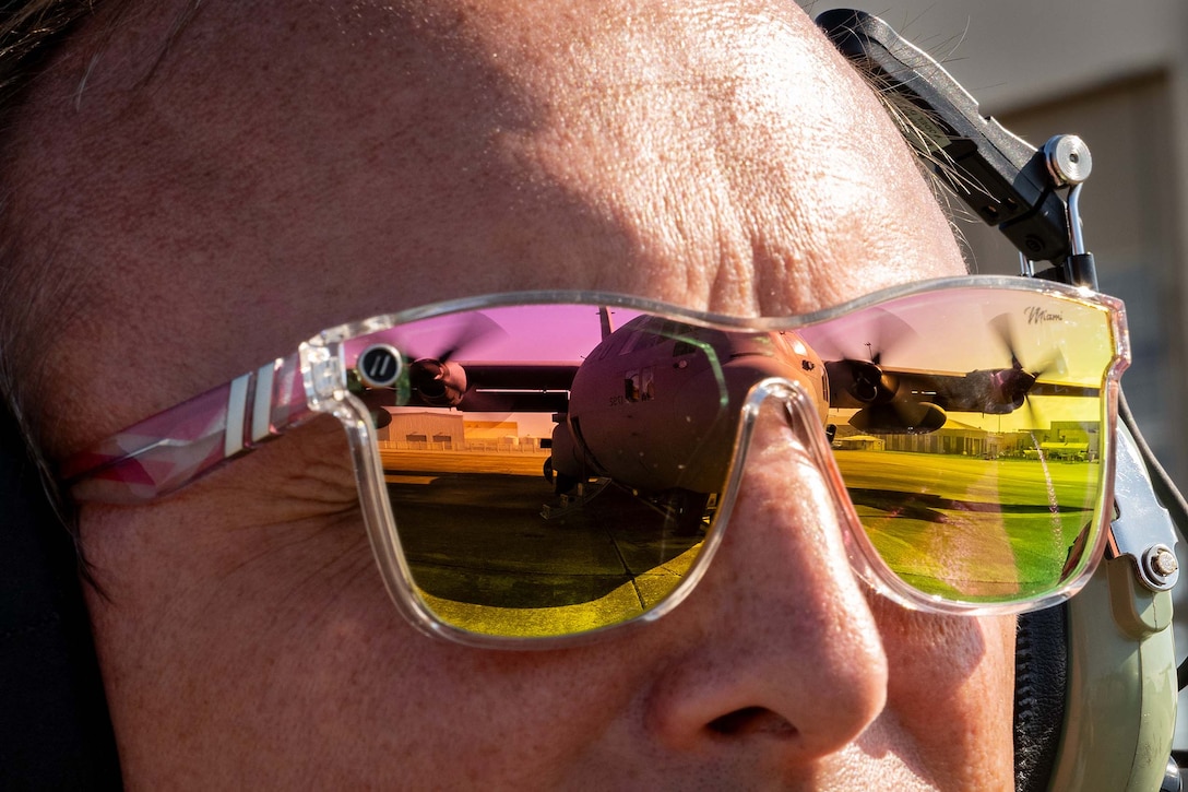 The reflection of a military aircraft is seen in an airman’s sunglasses in a close-up photo.