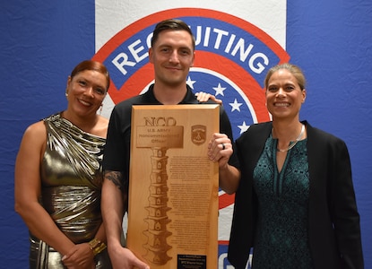 Three Soldiers pose with an award plaque in front of an Army Recruiting backdrop