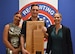 Three Soldiers pose with an award plaque in front of an Army Recruiting backdrop