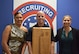 Three Soldiers smile and hold up an award plaque in front of an Army Recruiting Brigade backdrop